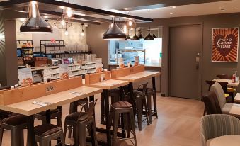 a restaurant with wooden tables and chairs , hanging lights , and a large window in the background at Premier Inn Caerphilly (Corbetts Lane)