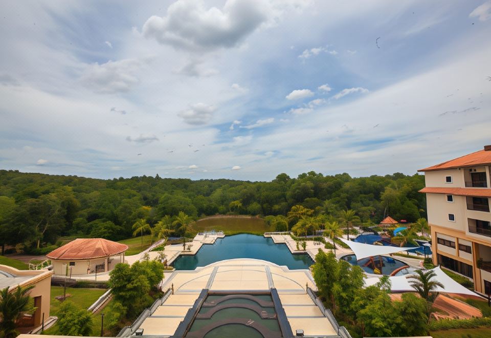 a bird 's eye view of a large swimming pool surrounded by trees and buildings , with blue skies overhead at Amverton Heritage Resort