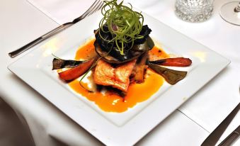 a white plate with a piece of salmon on top , surrounded by various vegetables and sauces at The Aston Motel Tamworth