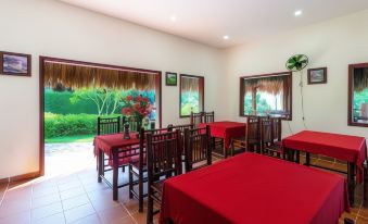 a dining room with red tables and chairs , surrounded by windows that offer views of the outdoors at Riverside Park Eco Resort
