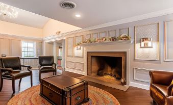 a cozy living room with a fireplace , a rug , and a trunk on the floor at The Aurora Inn Hotel and Event Center