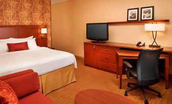 a hotel room with a king - sized bed , a desk , a television , and a chair at Courtyard Toledo Airport Holland