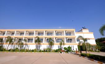 a large , white building with multiple floors and balconies , surrounded by palm trees and a parking lot at That Phanom River View Hotel
