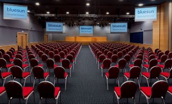 a large conference room with rows of red chairs arranged in an auditorium - style seating arrangement at Bluesun Hotel Elaphusa