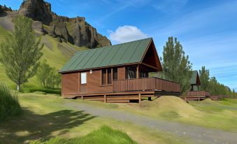 a brown wooden cabin with a green roof is nestled in a mountainous landscape under a clear blue sky at Hörgsland Cottages