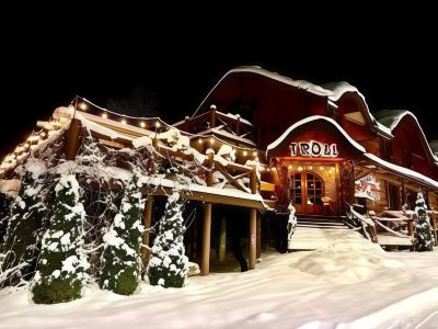 a snowy scene with a wooden building , possibly a hotel , surrounded by snow - covered trees and lit up at night at Troll