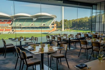 a restaurant with tables and chairs is shown with a large window overlooking a sports field at Oval Hotel at Adelaide Oval, an EVT hotel