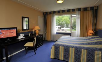 a hotel room with a blue and yellow color scheme , featuring a bed , desk , chair , and window at Fletcher Parkhotel Val Monte
