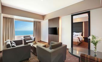 a modern living room with a large window offering an ocean view , featuring comfortable furniture and a flat - screen tv at Aston Kupang Hotel & Convention Center
