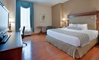 a large bed with white linens is in a room with wooden floors and a desk at Clayton Plaza Hotel & Extended Stay