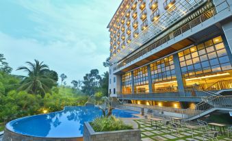 a large hotel with a pool and lounge chairs is surrounded by greenery , including palm trees at FamVida Hotel Lubuklinggau Powered by Archipelago