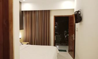 a modern hotel room with a white bed , brown curtains , and a tv on the wall at The Royal Joglo