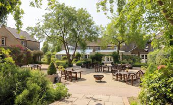 a courtyard with wooden tables and chairs , surrounded by trees and buildings , under a clear blue sky at The Barnsdale, Rutland