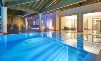 a modern villa with an indoor swimming pool and outdoor seating area , illuminated by the sun at Cascade Wellness Resort