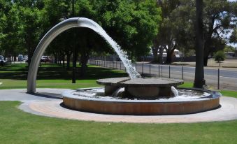 a water fountain in a park with a large archway above it , surrounded by green grass and trees at Keith Motor Inn