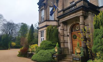 a large mansion with a blue and white flag hanging outside , surrounded by green grass and trees at Tre-Ysgawen Hall & Spa