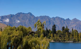 a serene landscape of a lake surrounded by trees and mountains , with a tree branch in the foreground at Lakeside Motel