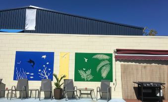 a building with three colorful paintings on its exterior , surrounded by patio furniture and a swimming pool at Black Marlin Motel