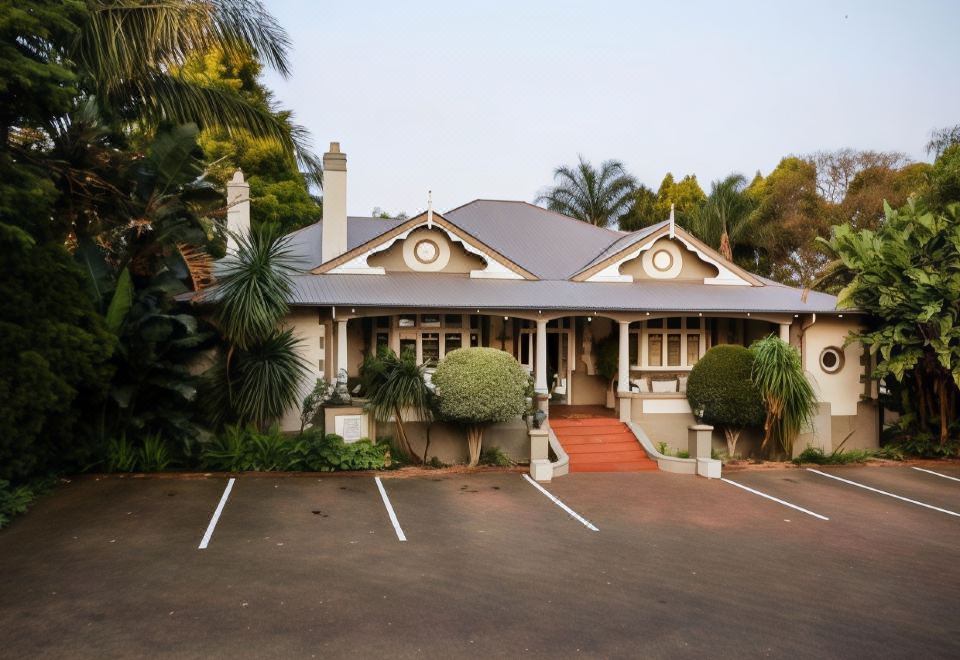 a large house with a red roof and white trim is surrounded by palm trees and bushes at Oxford Lodge Vryheid