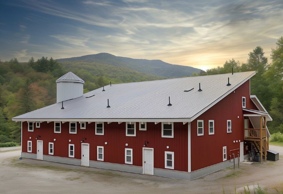 a red barn with a white roof and several windows is surrounded by trees , mountains , and sky at Mad River Lodge