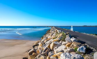 a beautiful beach scene with a rocky shoreline and a pier extending into the ocean at Iluka Motel