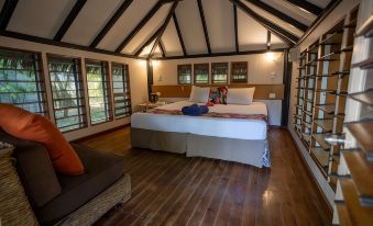 a bedroom with a wooden floor and ceiling , featuring a large bed and multiple windows at Likuri Island Resort Fiji