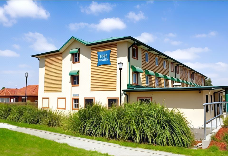 a modern building with a blue sign , surrounded by green grass and trees , under a clear blue sky at ibis budget Casula Liverpool