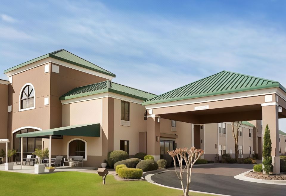 a large building with a green roof and multiple cars parked in front of it at Spring Lake Inn & Suites - Fayetteville