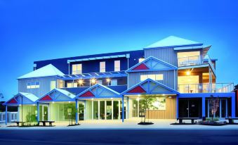 a large building with blue and white trim , a courtyard , and a few people in the parking lot at The Island Accommodation