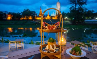 a wooden tray filled with food and a vase of flowers , placed on a dining table near a body of water at Sala Ayutthaya