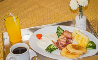 a plate of breakfast food , including eggs , bacon , and pancakes , is on a table with a cup of coffee and a glass of orange at Eurotel Angeles