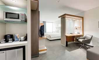 a modern hotel room with a kitchenette , bed , desk , and office area , all decorated in white and gray colors at SpringHill Suites Houston the Woodlands