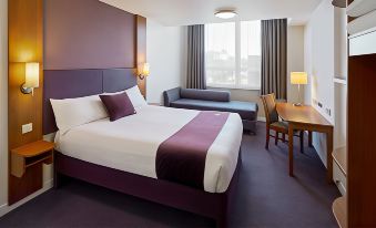 a large bed with a purple blanket and white sheets is in a room with a couch , table , and window at Premier Inn Penzance