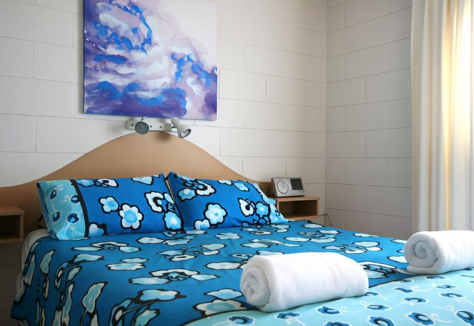 a cozy bedroom with a blue and white bedspread , a blue pillow , and a painting on the wall at Lake Edge Holiday Units