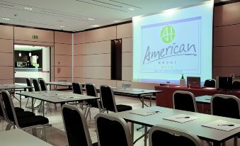 a conference room with rows of chairs arranged in a semicircle , and a projector mounted on the wall at American Hotel