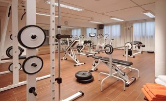 a well - equipped gym with various exercise equipment , including weightlifting machines and free weights , arranged on wooden flooring at B&B Hotel Bologna