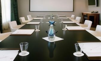 a conference room with a long table , chairs , and a projector screen displaying a movie at The Twelve Hotel