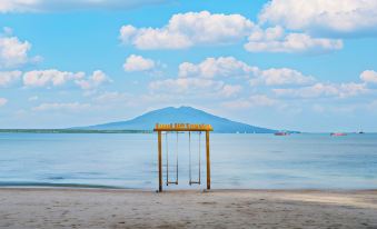 a swing set on the beach with a large mountain in the background and a blue sky above at Grand Elty Krakatoa
