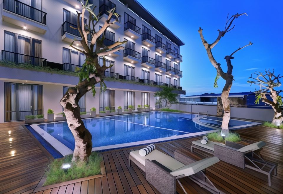 an outdoor pool surrounded by a wooden deck , with lounge chairs and umbrellas placed around the pool area at ASTON Inn Mataram