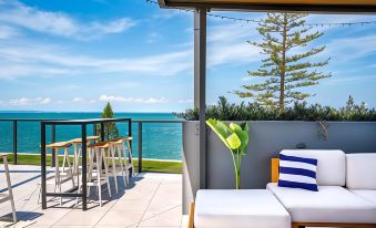 a beautiful outdoor terrace with a white and blue striped sofa , wooden chairs , and a view of the ocean at The Sebel Brisbane Margate Beach