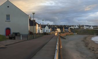 a paved walkway along the edge of a body of water , with several houses in the background at Castletown Hotel