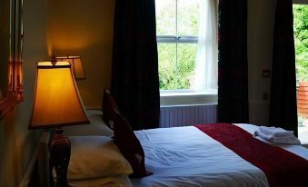 a well - lit hotel room with a bed , lamp , and window , giving a cozy and comfortable atmosphere at Old Posting House