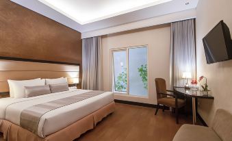 a modern hotel room with a large bed , wooden floors , and a balcony door leading to a green garden at Solaris Hotel Malang