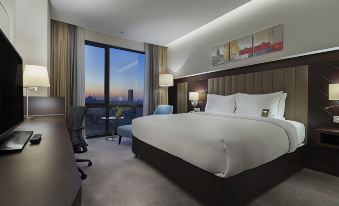 a large bed with white linens is situated in a room with a window overlooking the city at Doubletree by Hilton Istanbul Umraniye