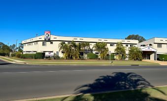 a large white building with a blue logo is surrounded by palm trees on the side of a road at Boulevard Lodge Bundaberg