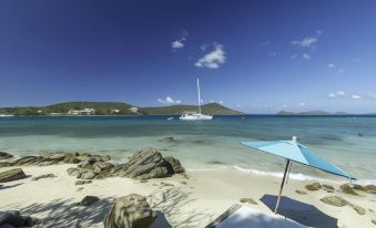 a sailboat is anchored in the ocean near a sandy beach , with a blue umbrella and a lounge chair nearby at Point Pleasant Resort