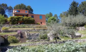 a large house with a red roof is nestled in a hillside , surrounded by trees and rocks at La Roque