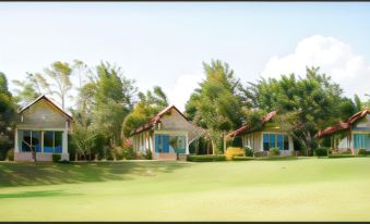 a grassy field with a row of two small houses , one on the left and the other on the right at Vimannam Resort