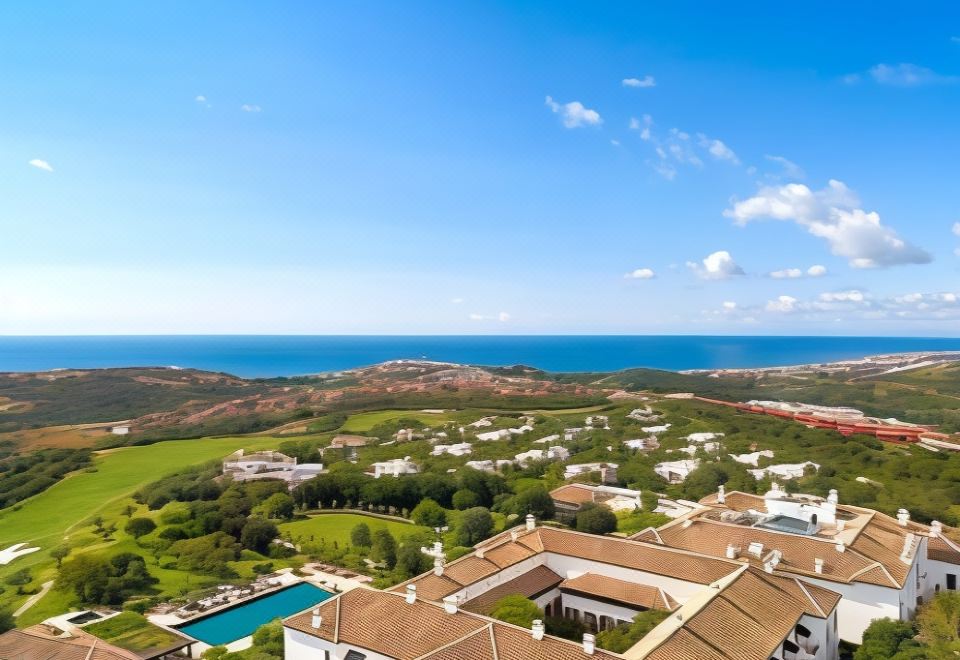 a large , white hotel with a brown roof is surrounded by lush greenery and overlooks the ocean at Finca Cortesin Hotel Golf & Spa