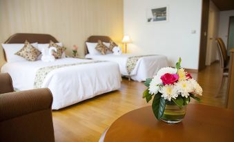 a bedroom with two beds , a table with a vase of flowers , and lamps on the wall at Thumrin Thana Hotel